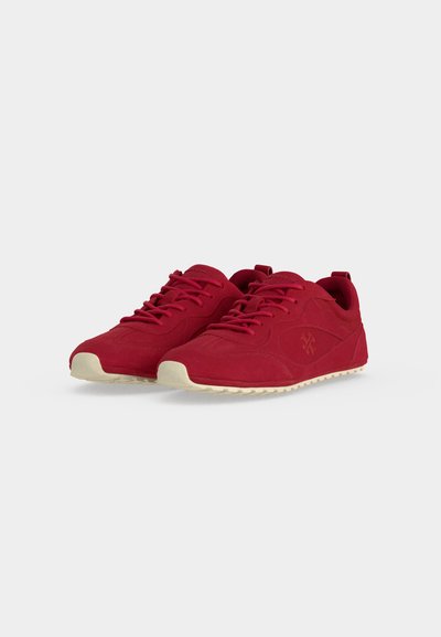 Paire de baskets rouges à lacets avec semelles beige et logo latéral discret sur un fond gris clair uni.