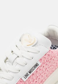 Biały sneaker z różową tkaną tkaniną, teksturowanym wzorem, płaskimi białymi sznurowadłami oraz złotym logo w kształcie serca na języku.