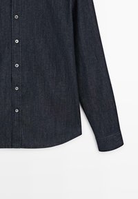 Camicia in denim scuro con chiusura frontale a bottoni, maniche lunghe e orlo curvo. Presenta bottoni argentati e tessuto con trama texturizzata.