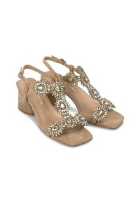 Sandales à talon bloc en suede beige avec un bout carré et des embellissements floraux décoratifs en cristal sur les brides. Bride de cheville ajustable incluse.