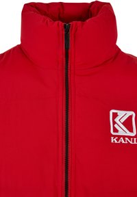 Rote Puffjacke mit hohem Kragen, schwarzem Reißverschluss und weißem gesticktem Logo. Glatte Stofftextur mit minimalen Nähten.