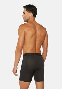 Zwarte boxershorts met een gladde textuur, met een donkere elastische tailleband met branding, weergegeven vanaf de achterkant. Brandweermanstijl knip.