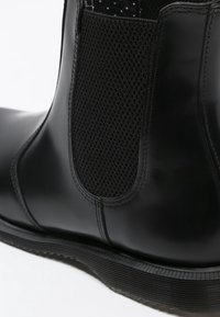 Botte Chelsea en cuir noir avec panneau latéral élastique texturé et semelle épaisse crantée, vue en gros plan de profil.