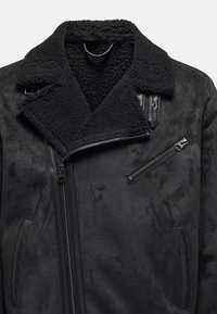 Schwarze Lammfell-Bikerjacke mit asymmetrischem Reißverschluss, strukturiertem Kragen, Schnallenriegel und brustseitiger Reißverschlusstasche.