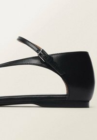 Black leather flat shoe with a narrow strap and adjustable buckle. Features an open side and a sleek, rounded toe design. Smooth texture.