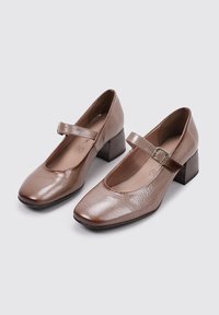Zapatos Mary Jane de cuero marrón con punta cuadrada, correa y tacón tipo bloque. La superficie presenta un acabado texturizado sutil.