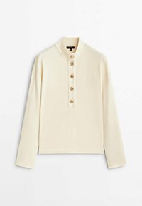 Camicia a maniche lunghe crema con colletto dritto e cinque grandi bottoni decorativi sulla pattina frontale, distesa su uno sfondo bianco.