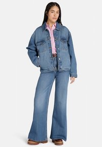 Jeansjacka i mellanmörkblått med avslappnad passform, två bröstfickor, kombinerad med ljusblå utsvängda jeans och en rosa skjorta med knappar. Brun bälte.