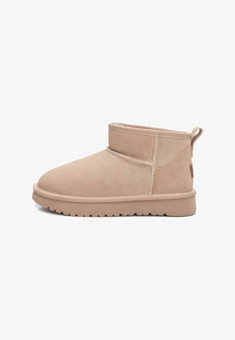 Botas por el tobillo de color beige claro, hechas de ante, con punta redondeada, detalles cosidos y una suela de goma texturizada con una lengüeta en la parte posterior.