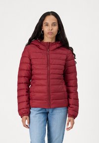 Rød polstret jakke med hette, med glidelås, elastiske mansjetter og kviltet tekstur. Brukt over blå jeans.