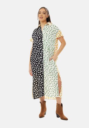 Shirt dress with a button-up collar; half black with white spots, half white with green spots and orange accents; side slits; worn with brown boots.