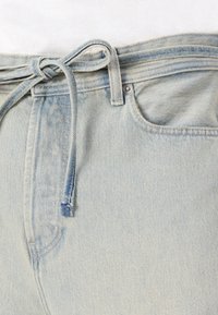 Lys blå denim jeans med snører, der har et fem-lommers design og en let slidt tekstur nær kanten.