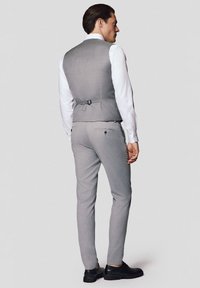 Szary dopasowany kamizelka z detalem w postaci paska, zestawiona z dopasowanymi spodniami. Model nosi białą koszulę i czarne buty.