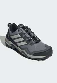 Scarpa da trekking grigia realizzata in materiali sintetici, con una tomaia in mesh testurizzato, suola in gomma, tre strisce nere e un sistema di allacciatura durevole.