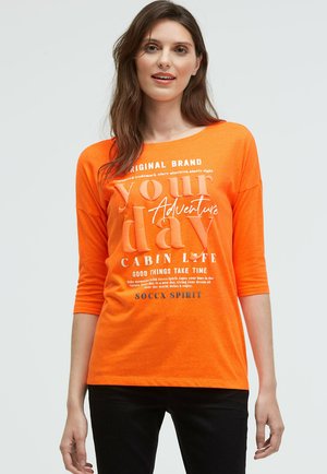 Oranges Langarm-T-Shirt mit weitem Ausschnitt, versehen mit weißem Text: "dein Abenteuer" und weiteren Phrasen; glattes, leichtes Material.