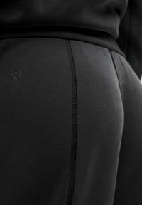 Sorte atletiske leggings med en tekstureret overflade, kontrasterende syninger og et lille logo. Stoffet ser strækbart og glat ud.