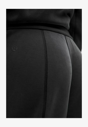 Mustad sportlikud retuusid, millel on tekstureeritud viimistlus, kontrastseid õmblusi ja väike logo. Kude tundub veniv ja sile.