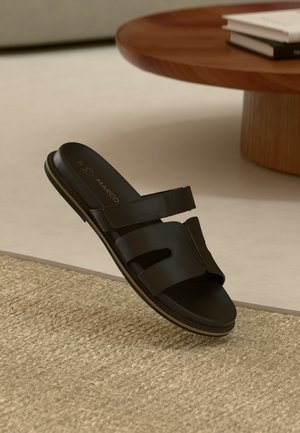 Sandale en cuir noir avec deux larges brides et un design à bout ouvert. Texture lisse avec un style minimaliste. Semelle fine avec un léger rebord.