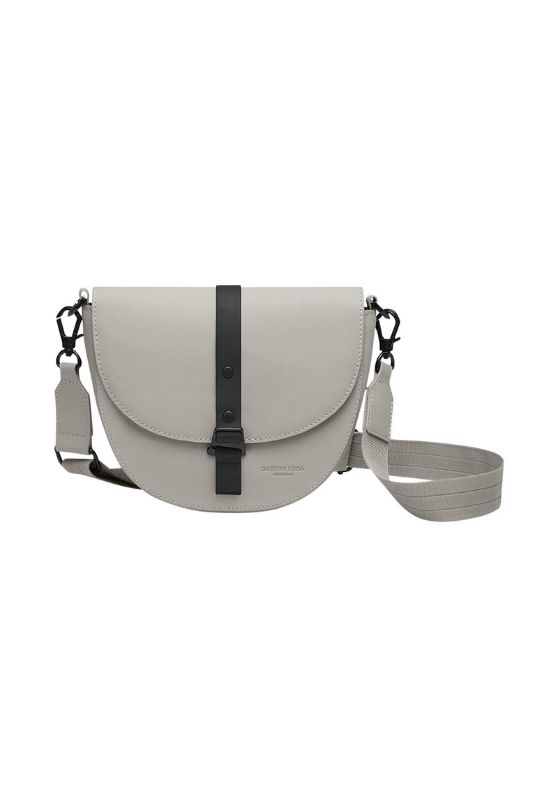 Grå läder crossbody-väska med ett runt lock, svarta remmar och justerbar axelrem. Har en logotyp på framsidan.