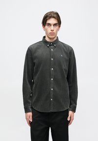 Szürke kordbársony gombos ing, terjedelmes gallérral, fehér gombokkal és kis logóval a mellrészen. Hosszú ujjú, textúrált anyag.