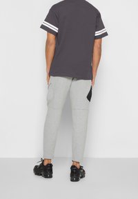 Šedé tričko s krátkým rukávem s bílými pruhy na rukávech, kombinované se šedými zúženými tepláky s černými bočními akcenty a černými teniskami.