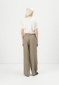 Cremfarbige Bluse mit kurzen Ärmeln und umgeschlagenen Manschetten, kombiniert mit hochgeschnittenen, weit geschnittenen olivgrünen Hosen, die eine glatte Textur und einen dezenten Glanz aufweisen.