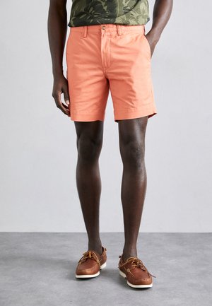 Herrliche pfirsichfarbene Baumwollshorts mit geradem Schnitt, seitlichen Taschen und Gürtelschlaufen. Getragen mit braunen Bootsschuhen.