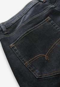 Pantalones vaqueros oscuros con un diseño de pierna recta, que cuentan con costuras naranjas, un único bolsillo trasero y una textura suave.