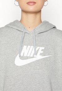 Grijze hoodie van een katoenmengsel, met een groot wit Nike-logo, een capuchon met trekkoord en geribde manchetten. Soepele textuur, casual pasvorm.