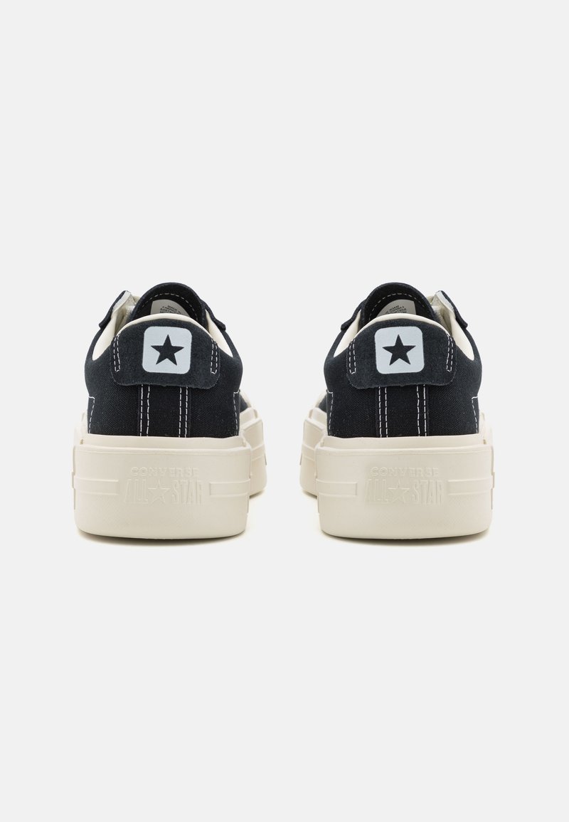 Czarne sneakersy na płaskiej podeszwie z białymi akcentami, z tylnym uchwytem z logo gwiazdy oraz fakturowaną białą podeszwą. Widoczne podwójne szwy po bokach.