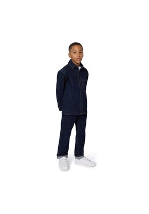 Veste en denim et ensemble de pantalons en bleu foncé, avec un devant à boutons et une poche poitrine. Associé à des sneakers blanches, se tenant sur un fond blanc.