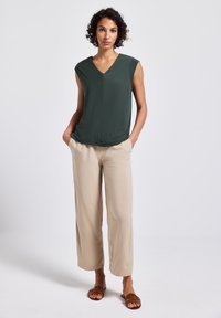 Top senza maniche verde scuro con scollatura a V, abbinato a pantaloni beige a gamba larga e sandali piatti marroni. Tessuto liscio con cuciture minime.
