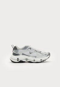 Adidași cu un upper din plasă gri și alb, talpă intermediară albă groasă, talpă exterioară texturată neagră și branding proeminent pe toc.