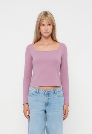 Haut court à manches longues en tissu violet clair avec un décolleté carré. Associé à un jean bleu clair à coupe décontractée.