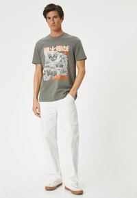 Grijs katoenen T-shirt met een grafisch ontwerp van karakters, oranje tekst met "TOKYO," gecombineerd met witte cargobroeken en lichte sneakers.