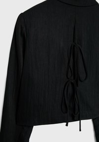 Veste noire à manches longues avec col, présentant deux nœuds noués au centre du dos.
