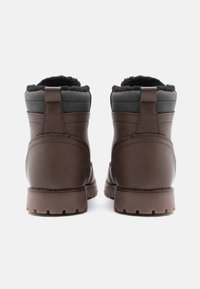 Hnedé kožené členkové topánky s umelým kožušinovým podšívkou, šedými tkaninovými akcentmi a robustnou gumovou podrážkou. Posilnená päta a pútko na jednoduché obúvanie.