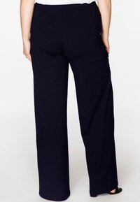 Zwarte wijde broek van zachte stof met een elastische tailleband, voorzien van een gladde textuur en een eenvoudige, verlengde silhouet.