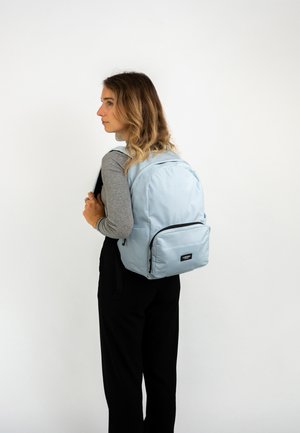 Sac à dos bleu clair en tissu, avec un grand compartiment principal et une poche frontale zippée, doté de bretelles noires ajustables.