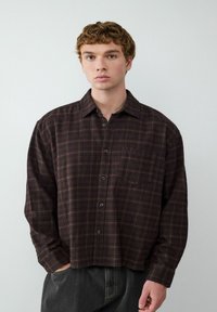 Braun kariertes Button-up-Hemd mit lockerer Passform, das über eine Brusttasche, schwarze Knöpfe und lange Ärmel verfügt. Strukturierten Stoff.