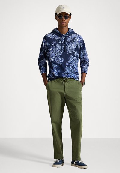 Ναυτικό φούτερ με λουλουδάτο σχέδιο, πράσινα παντελόνια, μπεζ καπέλο και γυαλιά ηλίου. Υφασμάτινη υφή, χαλαρή εφαρμογή και άνετα υποδήματα για μια ανέμελη εμφάνιση.