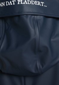 Matériau imperméable bleu marine à texture lisse, présentant un texte blanc audacieux le long du bord supérieur, indiquant une citation ou une phrase.