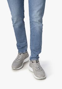 Zapatillas deportivas grises con una mezcla de ante texturizado y tela suave, con suelas blancas y acentos negros. Llevadas con unos vaqueros de color azul claro.