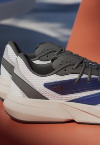 Athletic shoes featuring a white mesh upper with gray accents, blue detailing, and a cream midsole labeled "LIGHTSTRIKE."