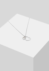 Sølv kædemand med en hjerteformet pendants outline og en rund sten accent, begge med en poleret finish og minimalistisk design.