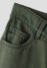 Pantalons vert olive avec une poche avant, une texture en denim robuste et des coutures visibles, dotés d'une passante de ceinture au niveau de la taille.
