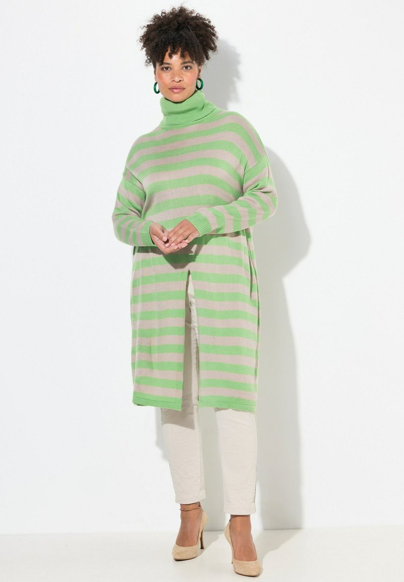 Maglione a righe sovradimensionato verde e beige con collo alto e fessure laterali, abbinato a pantaloni beige e tacchi nudi, caratterizzato da un maglione a punto testurizzato.