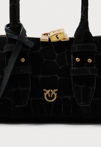 Juodas krokodilo odos tekstūros rankinukas su auksiniu paukščio emblemu ir spynos detale priekyje, turintis dvi viršutines rankenas ir odinį diržą.