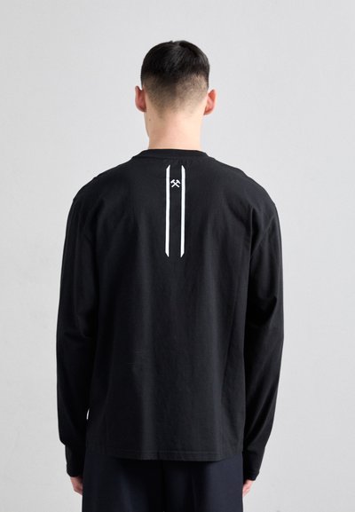 Musthave musta pika varrukaga T-särk, mille taga on minimalistlik valge graafika, ümmargune kaelus ja lõdvem mõõt.