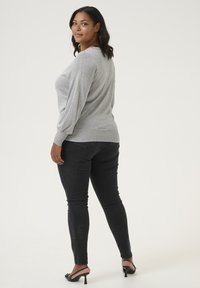 Svetl Gray pletený sveter s voľným strihom a balónovými rukávmi, skombinovaný s čiernymi skinny džínsy a čiernymi sandálmi na podpätku.